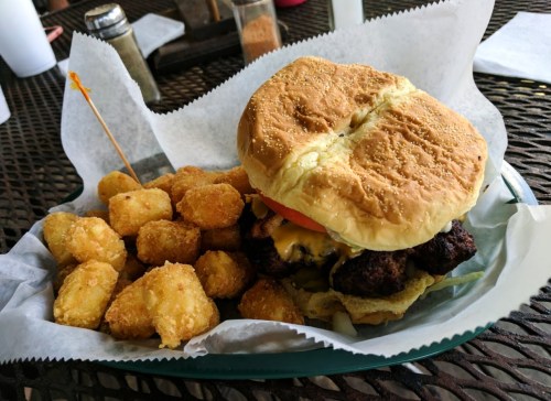 A juicy cheeseburger with a sesame seed bun, served with a side of crispy tater tots on a green plate.