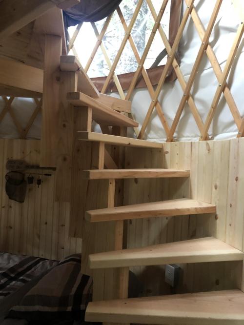 Wooden spiral staircase inside a cozy yurt, with natural light filtering through the windows.