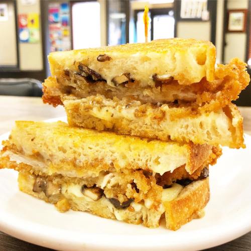 A stacked grilled cheese sandwich with crispy golden bread and melted cheese, served on a white plate.