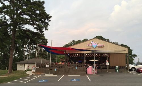 A restaurant with a colorful awning, surrounded by trees and parking spaces, under a cloudy sky.