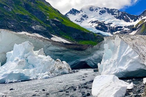 A stunning glacier landscape with towering ice formations, a river, and snow-capped mountains under a blue sky.