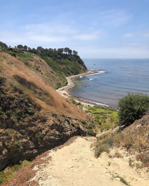 A scenic coastal view with cliffs, greenery, and calm waters under a clear blue sky.