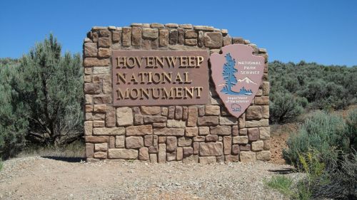 Sign for Hovenweep National Monument, featuring stone structure and National Park Service logo against a clear blue sky.