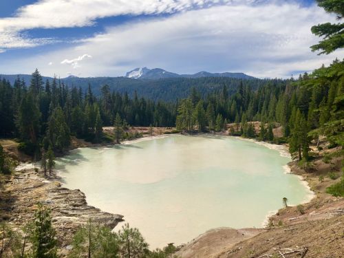 A serene lake surrounded by trees and mountains under a partly cloudy sky.