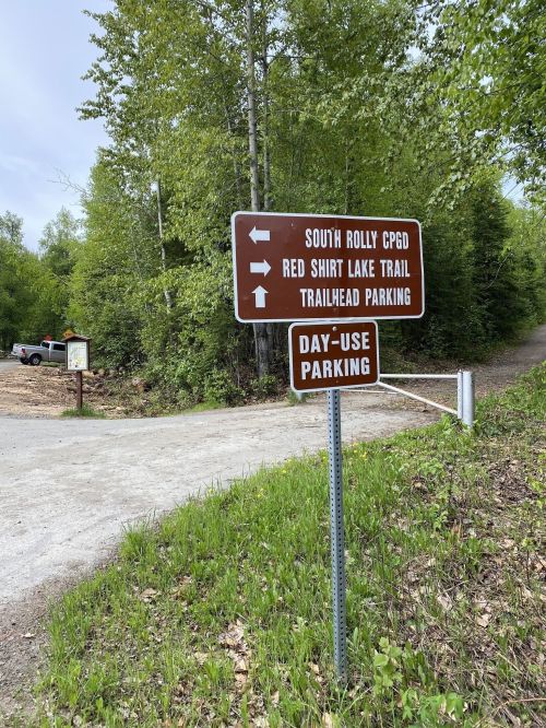 Signpost indicating directions to South Rolly CPGD, Red Shirt Lake Trail, and day-use parking in a wooded area.