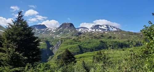A scenic view of snow-capped mountains surrounded by lush green hills and a clear blue sky.