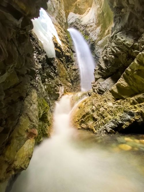 A serene waterfall cascades down rocky cliffs into a tranquil pool, surrounded by rugged stone formations.