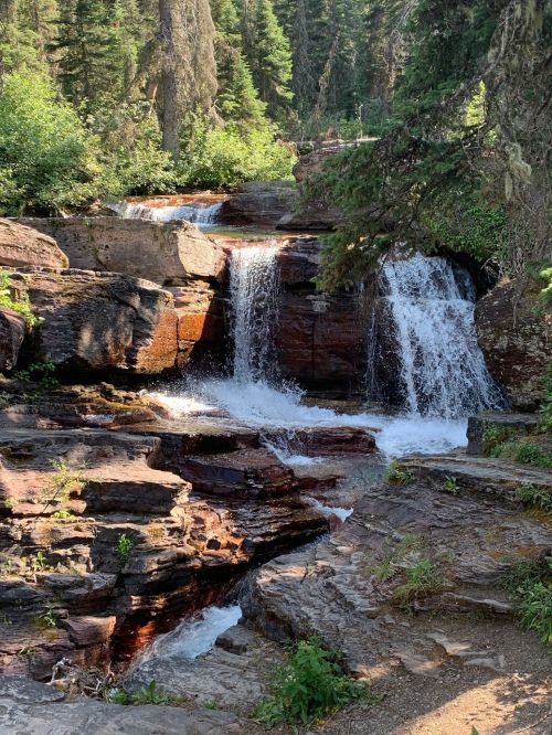 A serene waterfall cascading over rocky terrain, surrounded by lush green trees in a natural setting.