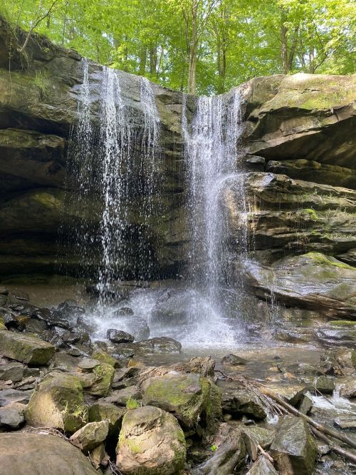 A serene waterfall cascading over rocky cliffs, surrounded by lush green foliage and a tranquil stream below.
