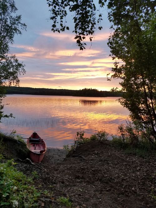 A serene lakeside scene at sunset, with a red kayak on the shore and colorful reflections on the water.