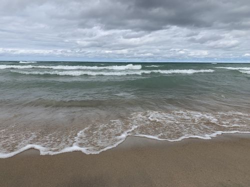 Waves gently lap at a sandy beach under a cloudy sky, creating a serene coastal scene.