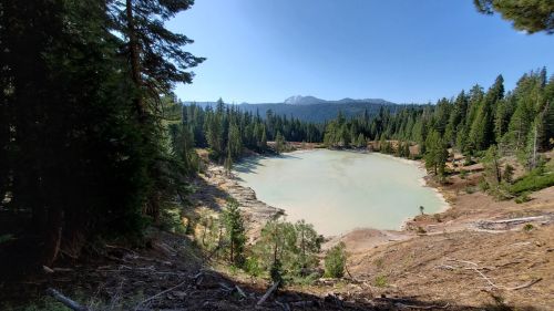 A serene lake surrounded by tall trees and mountains under a clear blue sky.