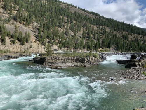 A scenic view of a river with rushing water, surrounded by rocky formations and lush green trees on the hillside.