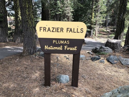Sign for Frazier Falls in Plumas National Forest, surrounded by trees and rocky terrain.