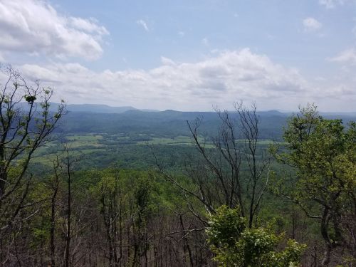 A panoramic view of lush green mountains and valleys under a partly cloudy sky.
