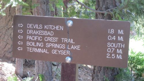 Trail sign indicating distances to various locations: Devils Kitchen (1.8 mi), Drakesbad, Pacific Crest Trail (0.4 mi), Boiling Springs Lake (0.7 mi), Terminal Geyser (2.5 mi).