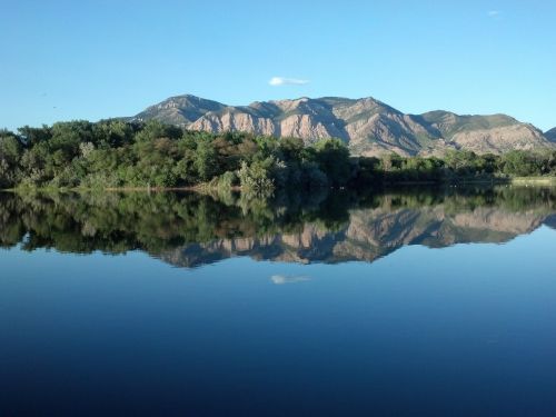 A serene lake reflecting mountains and lush greenery under a clear blue sky.