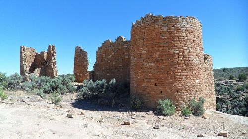 Ancient stone ruins with circular structures, surrounded by sparse vegetation under a clear blue sky.