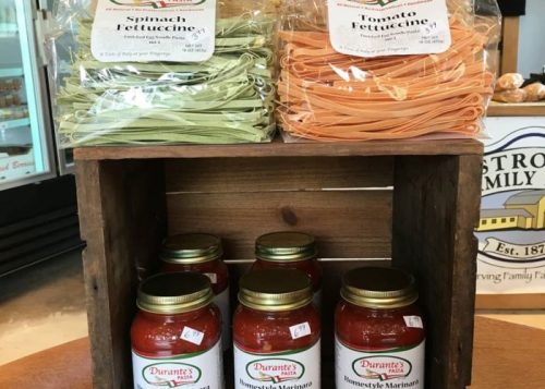 A wooden crate displays packages of spinach and tomato fettuccine, with jars of marinara sauce below.