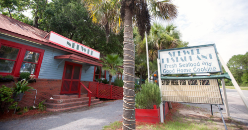 Exterior of a seafood restaurant with a sign advertising fresh seafood and home cooking, surrounded by palm trees.