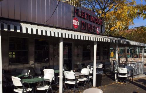 Exterior of Fleetwood Diner with outdoor seating, a striped awning, and autumn leaves in the background.