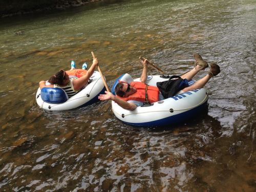 Two people relax on inflatable tubes in a river, enjoying a sunny day while holding paddles.