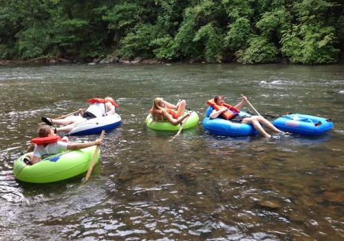 Four people relax on colorful inner tubes in a river, surrounded by lush greenery.