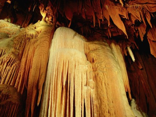 Stalactites and stalagmites in a cave, showcasing intricate formations and warm earthy tones.
