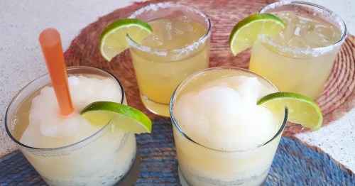 Four refreshing cocktails with lime slices and salt rims, served on colorful woven placemats.