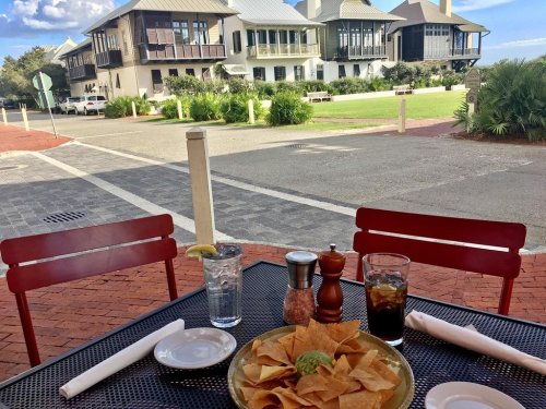 A table set with nachos, drinks, and a view of a charming street and large houses in the background.