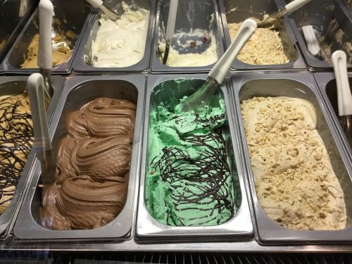 A display of various gelato flavors in metal containers, including chocolate, mint, and vanilla.