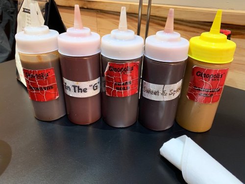 Five squeeze bottles of sauces with labels, arranged on a table. The sauces include various flavors for dipping.