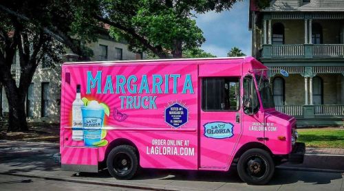 A bright pink food truck with "Margarita Truck" written on the side, parked under trees.