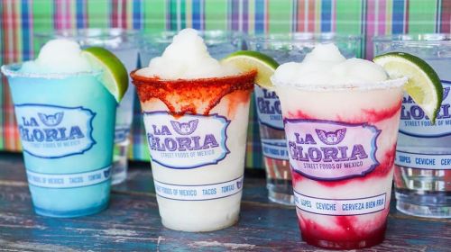 Colorful frozen drinks in cups with lime slices, featuring vibrant flavors and a festive presentation.
