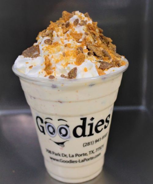A creamy dessert in a cup topped with whipped cream and crushed toppings, featuring the logo "Goodies" on the side.