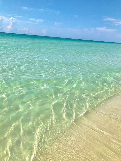 Clear turquoise water gently laps at a sandy beach under a bright blue sky.