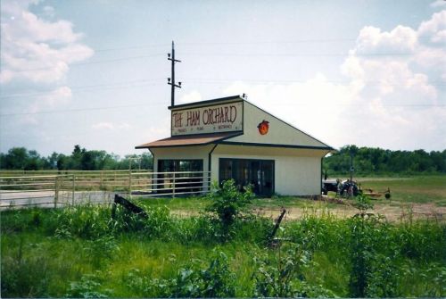 A small building labeled "The Jam Orchard" surrounded by green grass and a fence under a blue sky.