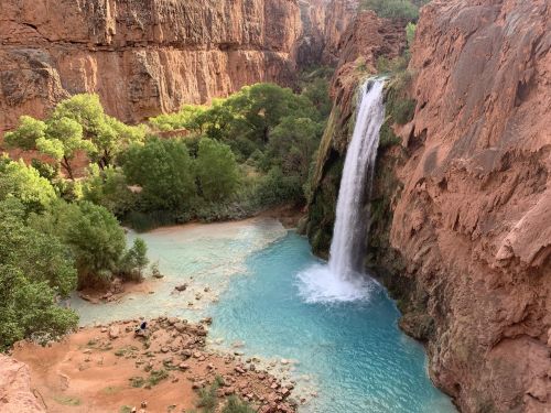 A stunning waterfall cascades into a turquoise pool surrounded by lush greenery and red rock formations.