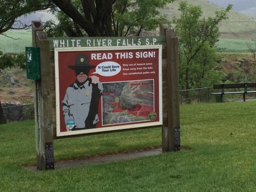 Sign at White River Falls State Park warning visitors to stay away from hazardous areas near the falls for safety.