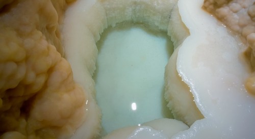 A close-up of a mineral formation with a small, clear pool of water surrounded by textured, creamy-colored rock.