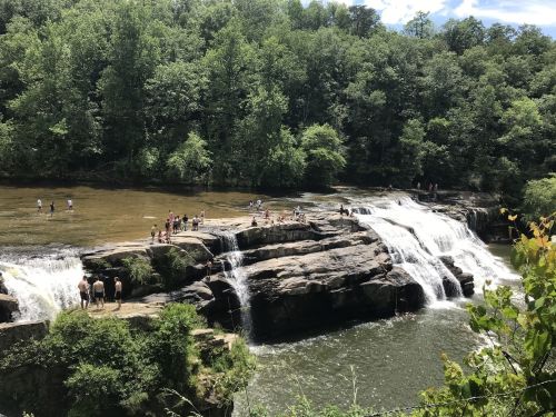 A scenic waterfall surrounded by lush greenery, with people enjoying the water and rocks below.