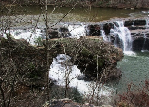 A scenic view of a waterfall cascading over rocks, surrounded by bare trees and a flowing river.
