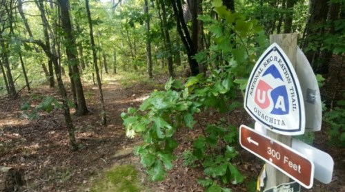 Trail sign for the Ouachita National Recreation Trail, surrounded by lush green trees and foliage.