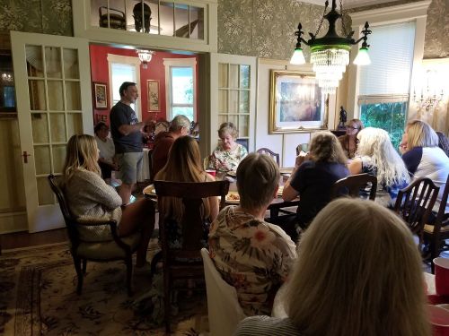 A group of people gathered around a dining table in a warmly lit room, engaged in conversation and enjoying food.