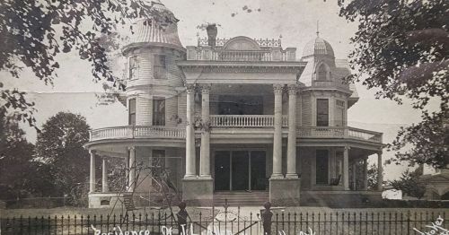 Historic Victorian mansion with ornate architecture, large porch, and decorative turrets, surrounded by trees.