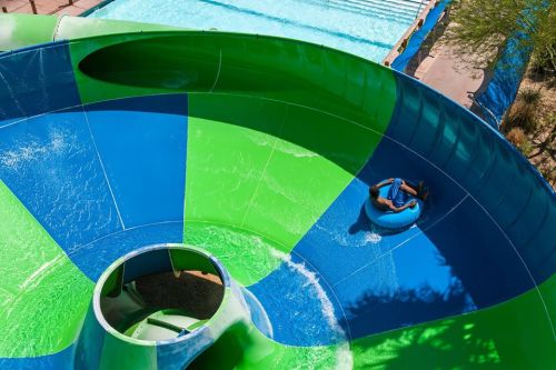 A person in a blue inner tube slides down a colorful water slide, with a pool visible in the background.