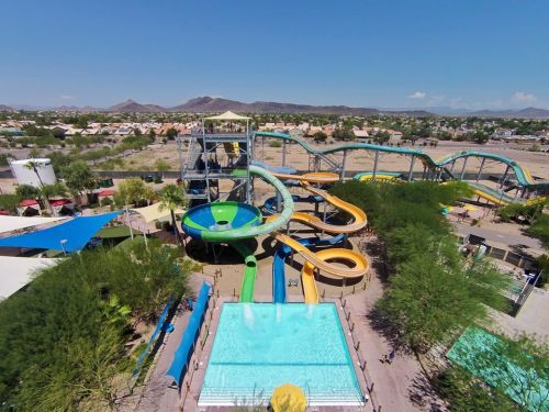 Aerial view of a water park featuring slides, a pool, and surrounding greenery under a clear blue sky.