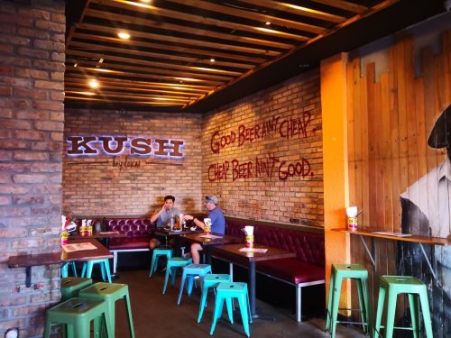 Cozy restaurant interior with brick walls, red seating, and green stools; two patrons sitting at a table.