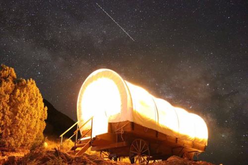A brightly lit covered wagon under a starry night sky, with a shooting star visible above.
