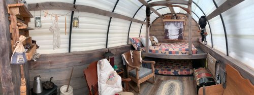 Cozy interior of a rustic cabin with a bed, vintage decor, and wooden furnishings, featuring warm, inviting textures.